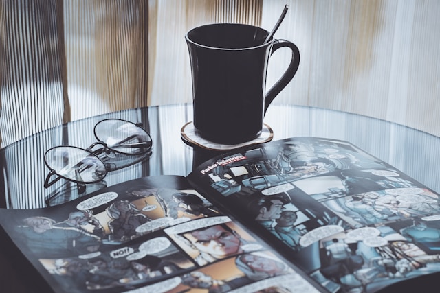 A Comic Book on a Table Next to Glasses and a Cup